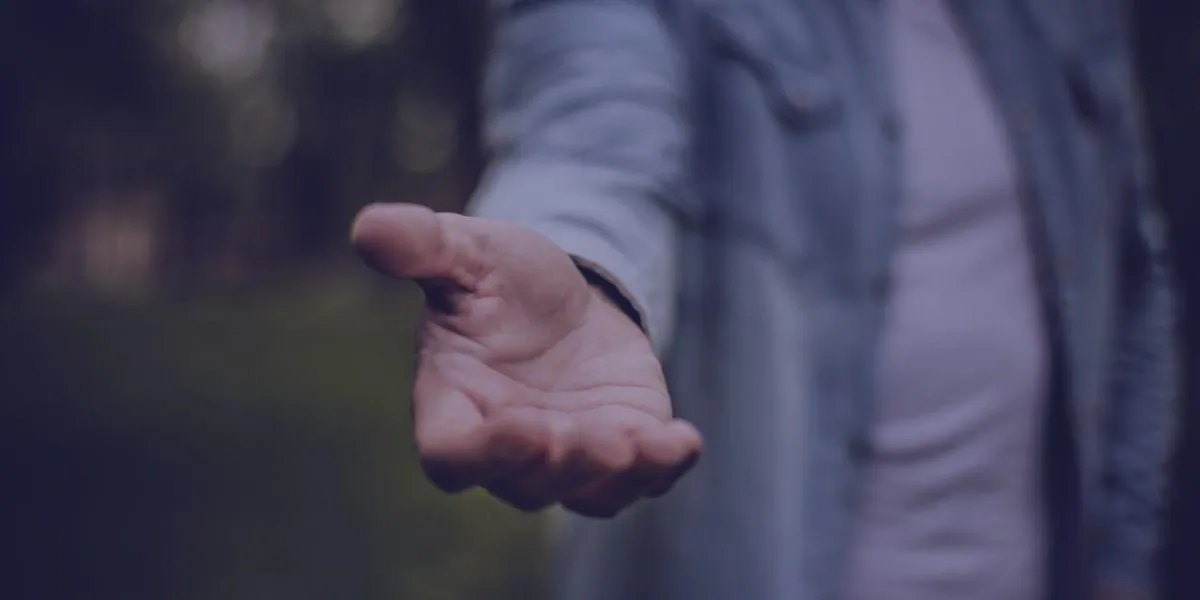 A hand reaches out towards the viewer with a blurred background.