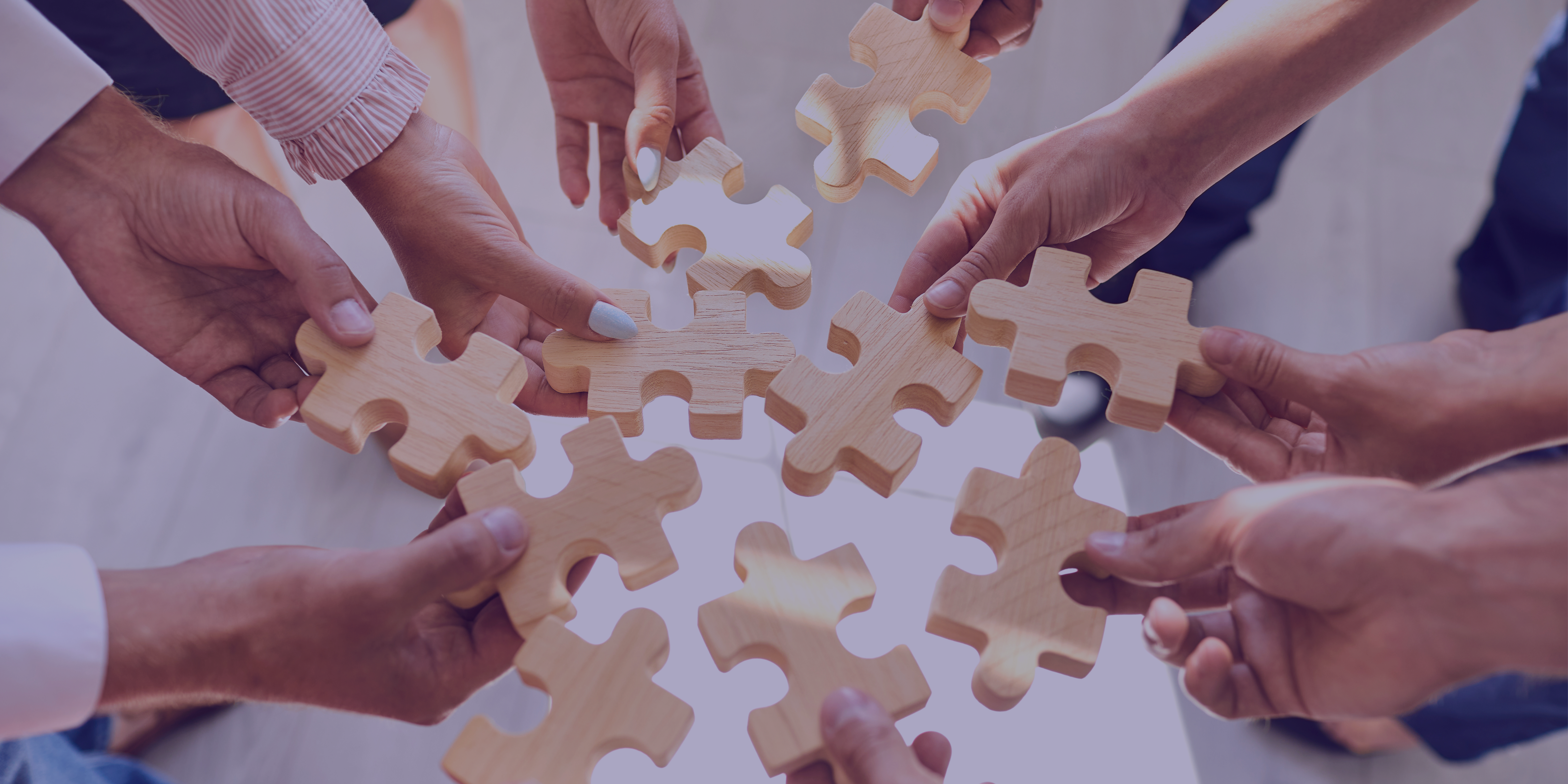 Team members holding wooden puzzle pieces together, symbolizing collaboration and teamwork