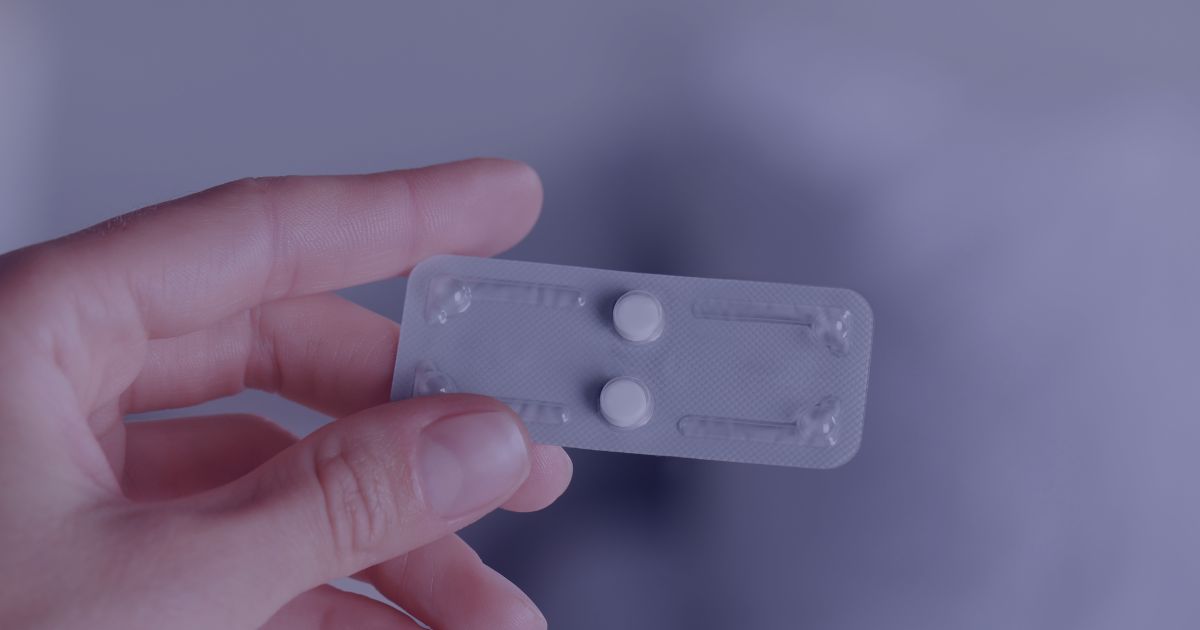 Hand holding a blister pack containing two emergency contraception pills.