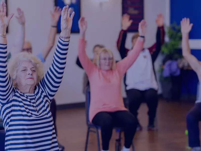 a group of older people undertaking chair based exercises to improve strength and balance