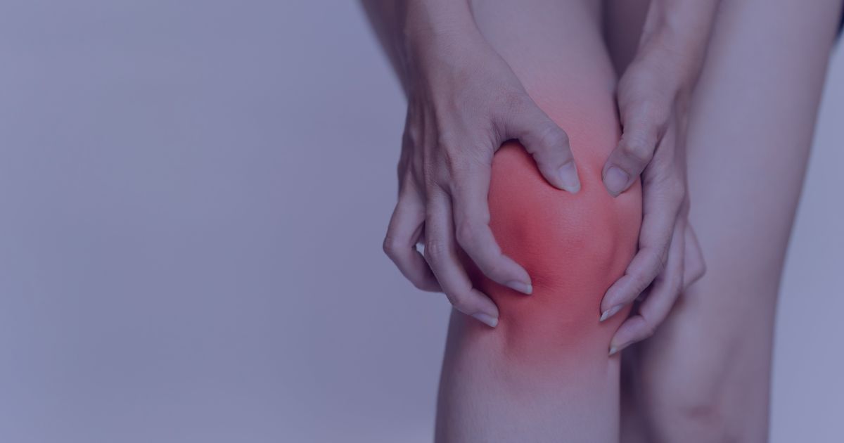 a women holding her knee which appears to be sore and inflamed. The image is overlaid with a blue filter.