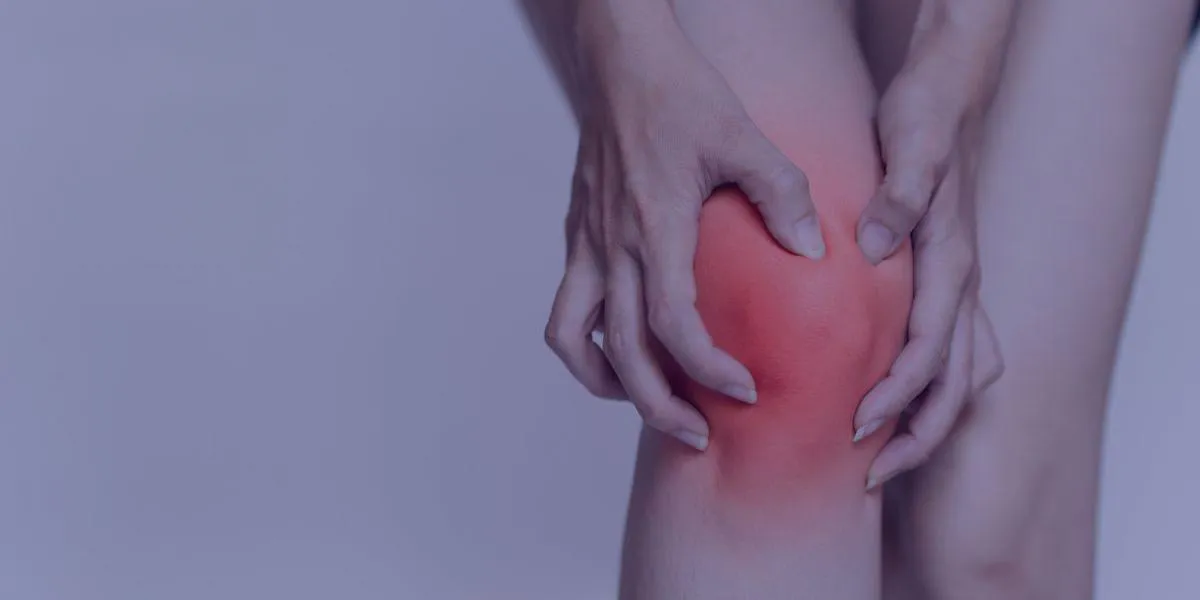 a women holding her knee which appears to be sore and inflamed. The image is overlaid with a blue filter.