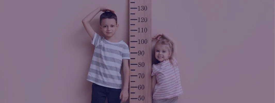 two young children stood either side of a large ruler measuring their growth