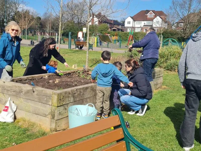 adults and children gather around a planter in a local park