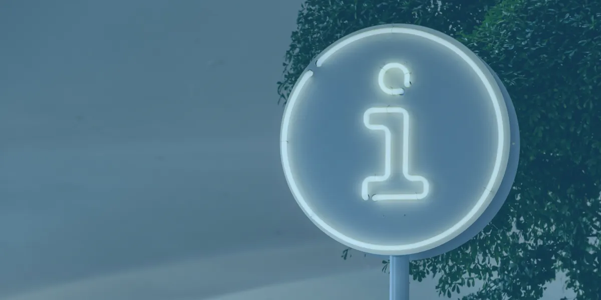 Illuminated information symbol sign in a circular frame, positioned near green foliage