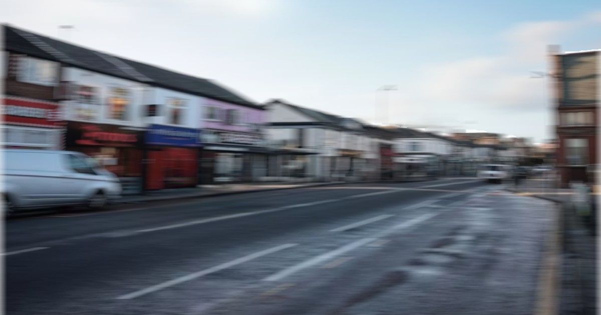 a blurred image of a main road lined with shops and takeaway outlets