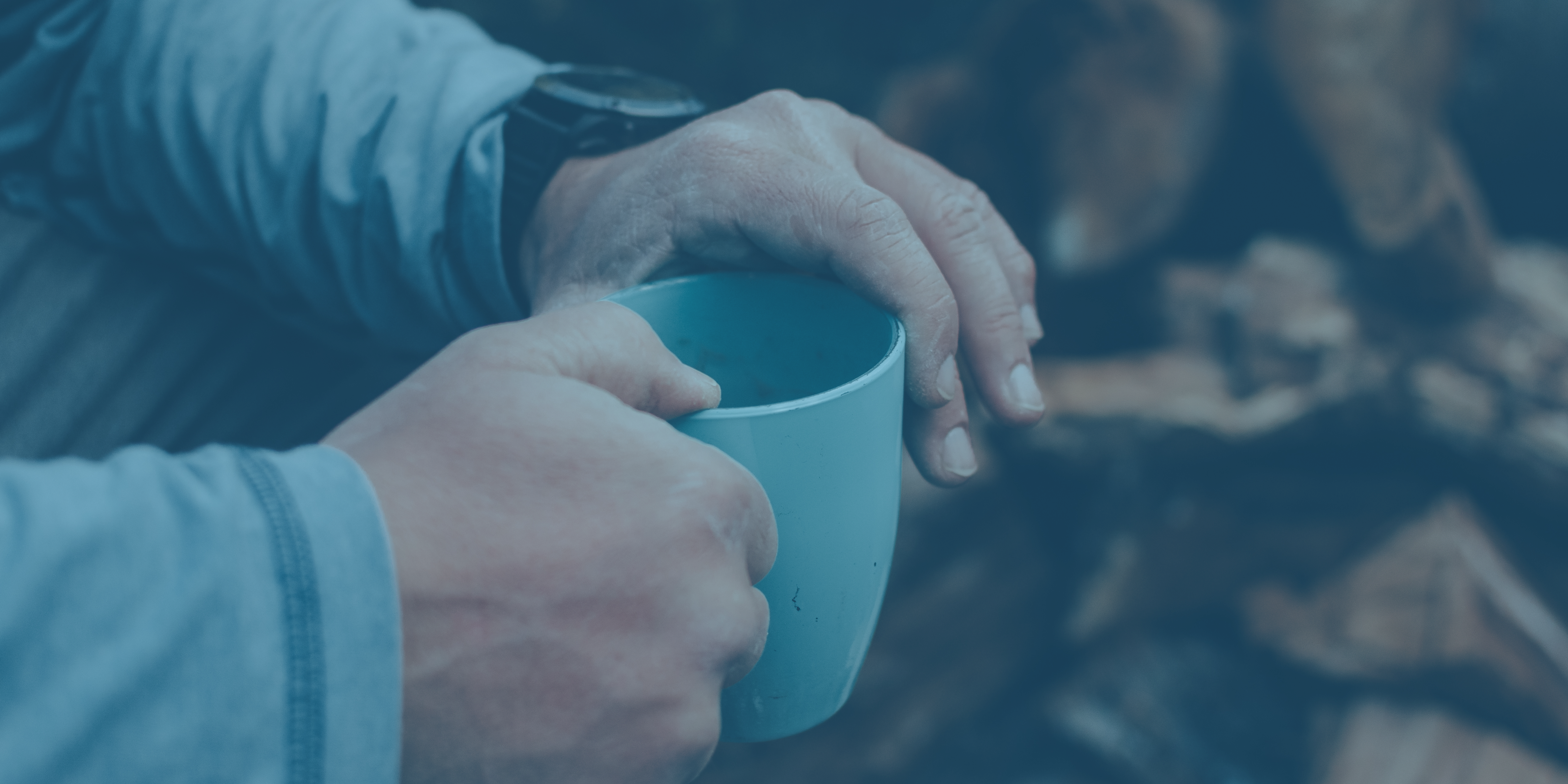 hands holding a light blue mug, with a wristwatch visible and chopped wood in the background